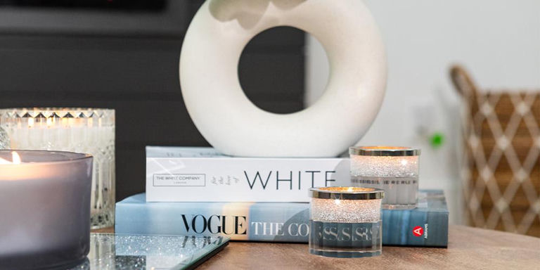 Candles, stacked books, and a sculptural vase styled on a mirrored tray