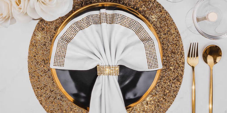 Black and gold place setting with beaded placemat and white napkin in a rhinestone ring