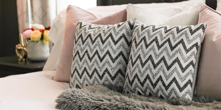 Two silver chevron rhinestone pillows layered on a soft pink bedroom bed