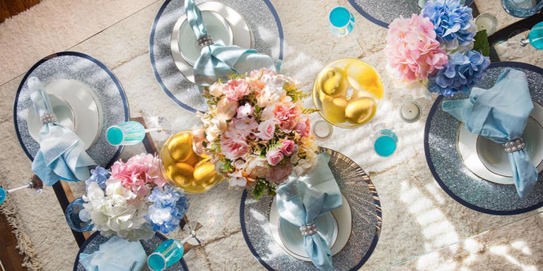 Overhead view of a spring table with blue napkins, silver chargers, and pastel flowers