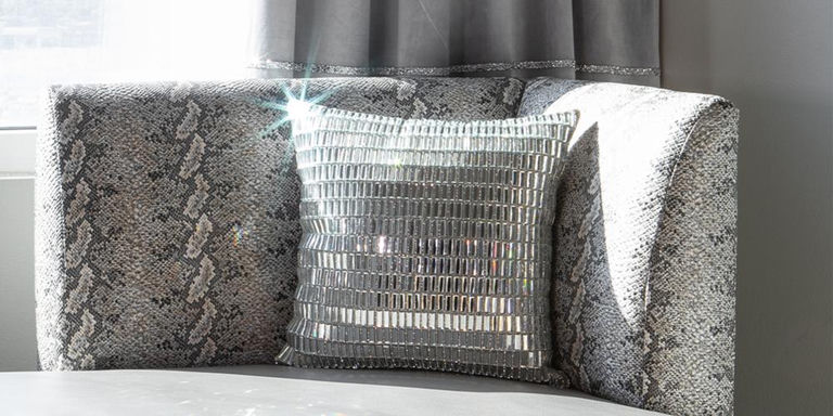 Silver mirrored accent pillow on a gray patterned sofa