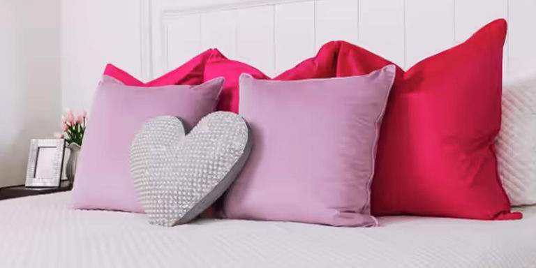 Heart-shaped pearl accent pillow on a bed with pink and fuchsia cushions