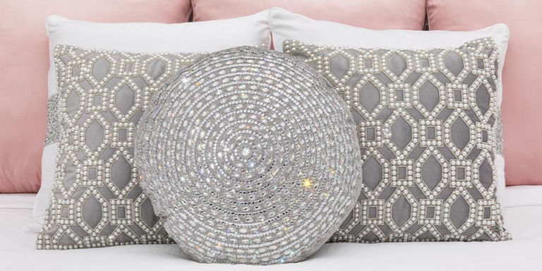 Round crystal accent pillow layered over silver patterned pillows on blush bedding