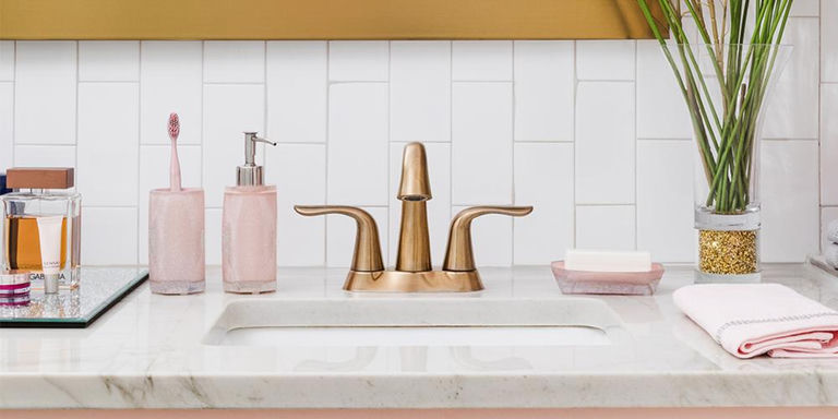 Bathroom vanity with pink bath accessories, gold faucet, and white subway tile