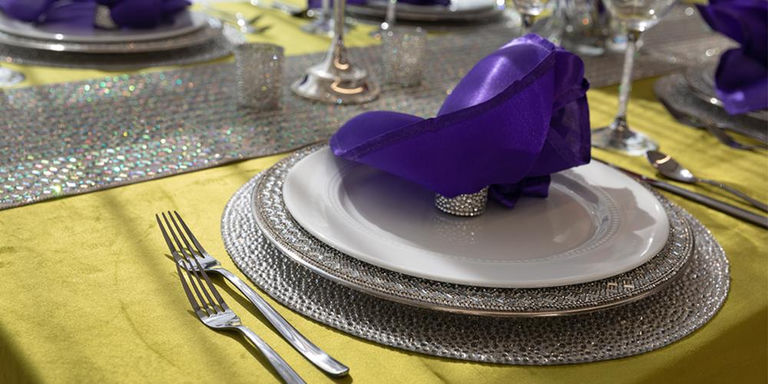 Silver beaded place setting with a purple napkin on a yellow tablecloth