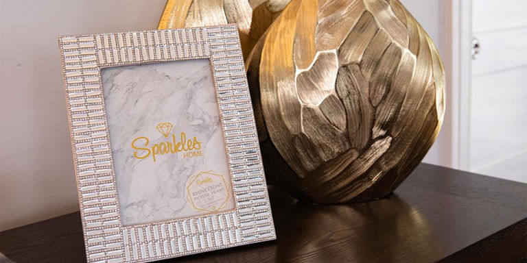 Jeweled photo frame beside a textured gold vase on a dark tabletop