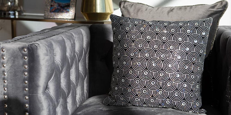 Black beaded accent pillow with circular pattern on a gray velvet chair