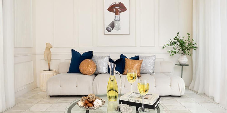White living room with navy and metallic accent pillows and wine on a glass table
