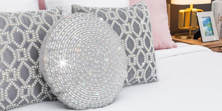 Round beaded accent pillow layered with lattice pillows on a white bed