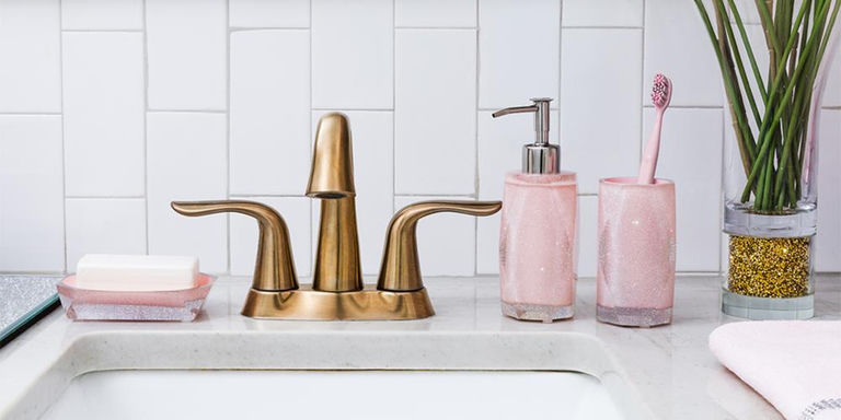 Pink glitter bath accessories beside a brass faucet on a white sink
