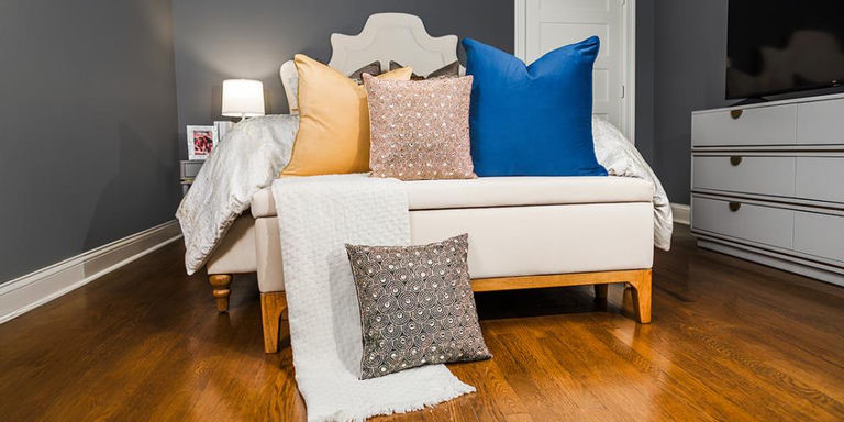 Dormitorio de lujo con almohadas decorativas en capas con texturas de melocotón, cuentas doradas y azul sobre una cama blanca