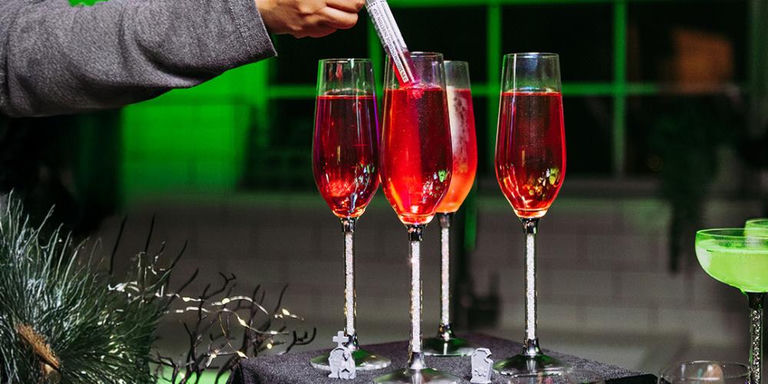 Three crystal-filled stem glasses with red cocktails and syringe garnish on dark Halloween table