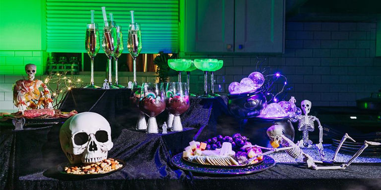 Spooky Halloween party table with skeleton decorations, crystal glasses, cocktails, and purple lighting effects