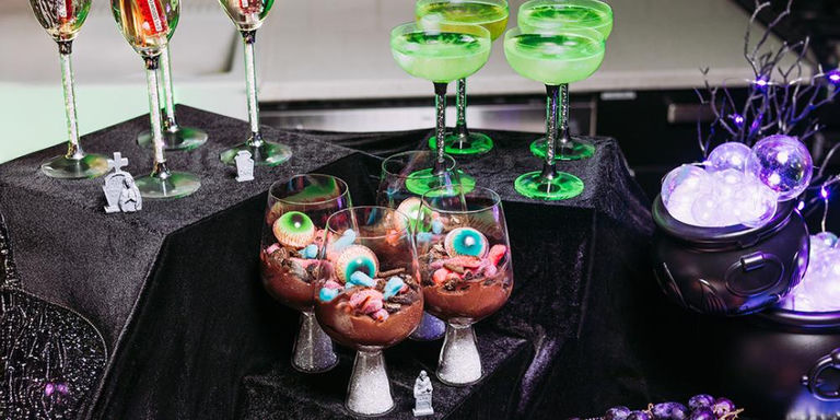Halloween dessert table with crystal stemware, green cocktails, chocolate mousse with edible eyeballs, and spooky decorations