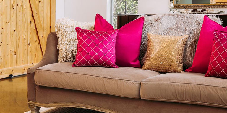 Canapé taupe décoré de coussins superposés en velours rouge, perles dorées et motifs décoratifs