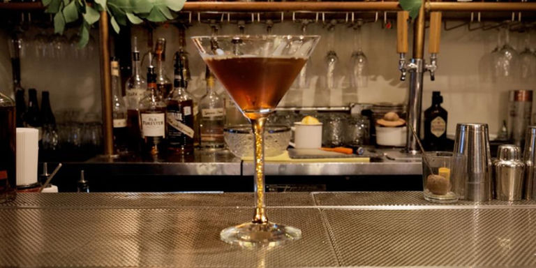 Classic Manhattan cocktail in crystal-filled stem martini glass with cherry garnish and candlelight