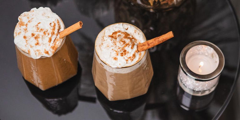 Pumpkin spice iced coffee in geometric gold-rimmed prism glass with whipped cream topping