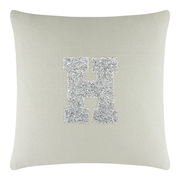 Square pillow in light green linen with a textured surface featuring a silver rhinestone monogram "H" in the center.