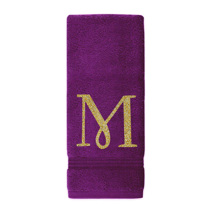 Purple cotton terry hand towel with a glittering gold rhinestone monogram "M" and a textured band at the bottom.
