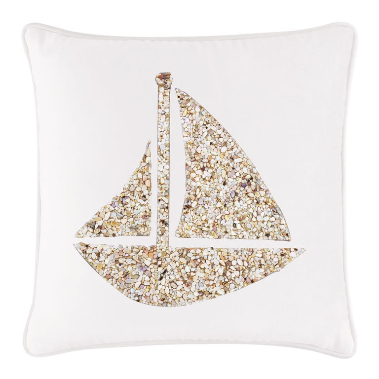 White velvet pillow featuring a seashell sailboat design made of beige and cream textured stones.