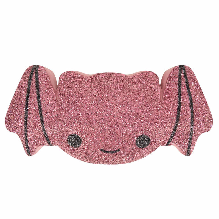 Pink bat-shaped pillow covered in glitter with black accents and a smiling face featuring a soft texture and rounded wings.