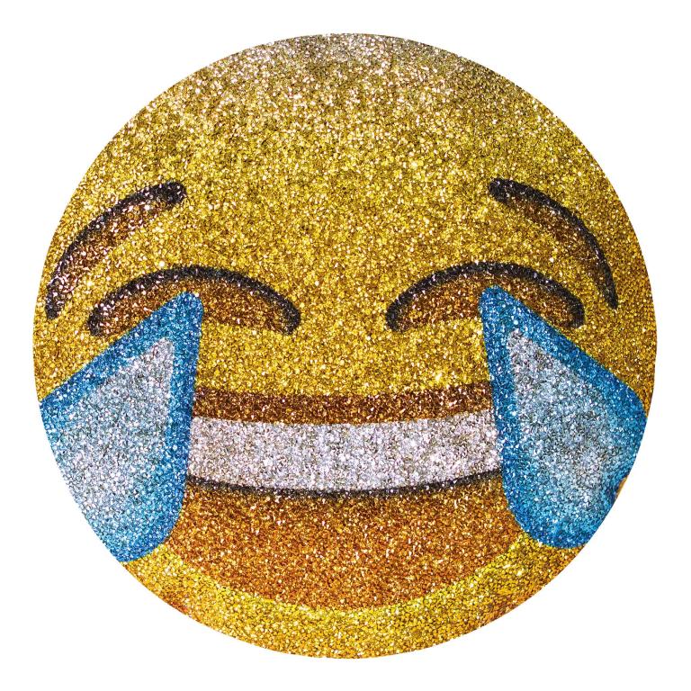Round pillow shaped like a laughing emoji featuring a glittery gold surface blue tears and a wide smiling mouth with black details.