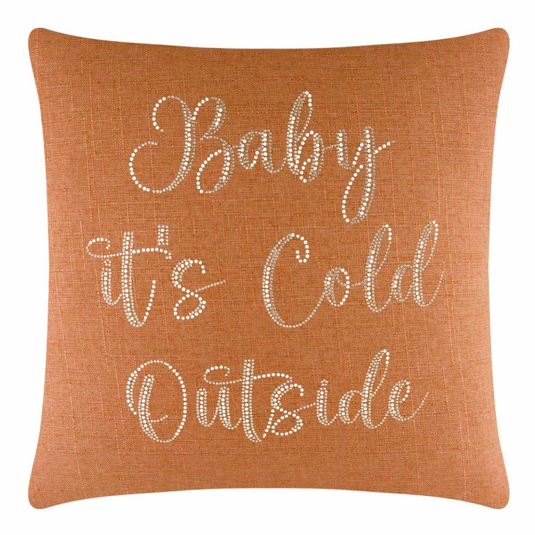 Square orange pillow with glass rhinestone lettering saying "Baby it's Cold Outside" on a textured fabric surface.