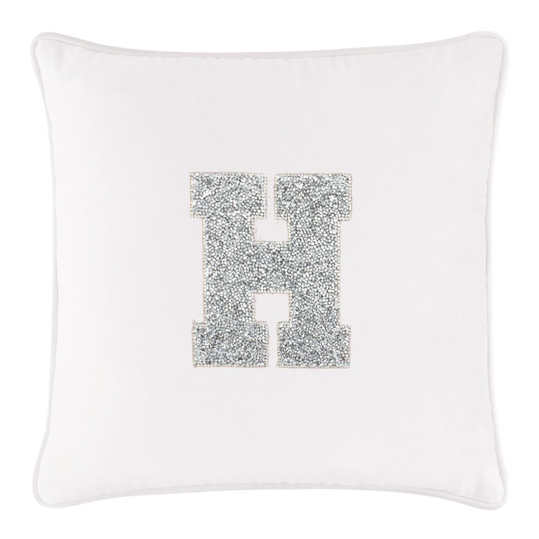 White velvet pillow featuring a large rhinestone-embellished letter "H" in silver with a piped edge.