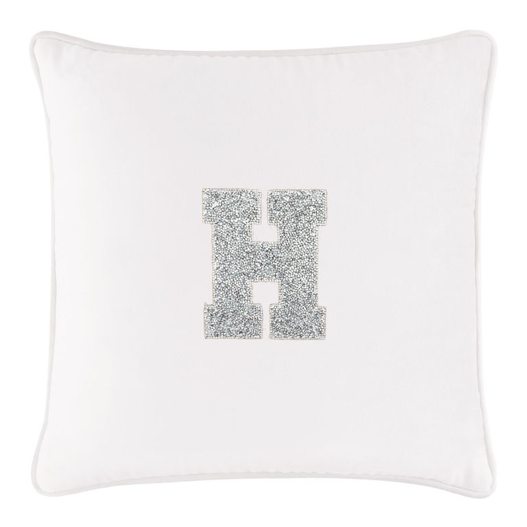 White velvet pillow featuring a silver rhinestone monogram "H" in the center with a piped edge.