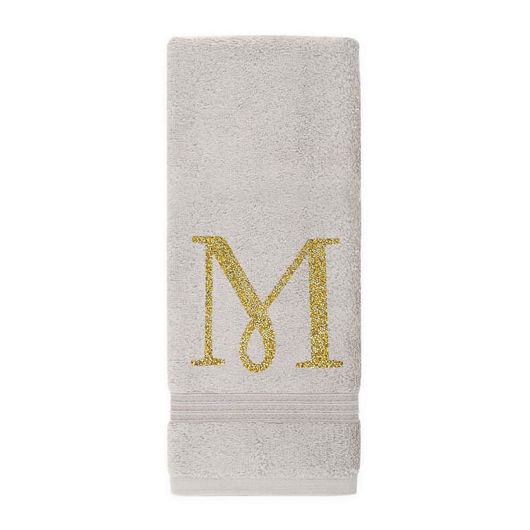 Gray plush cotton terry hand towel with a gold rhinestone monogram "M" and a textured band at the bottom.