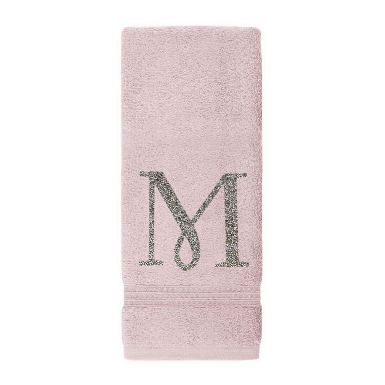 Plush pink cotton terry hand towel with a sparkling rhinestone monogram "M" and decorative horizontal stripes at the bottom.