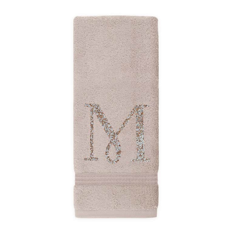 Taupe cotton terry hand towel with a rhinestone monogram "M" and a textured border at the bottom.