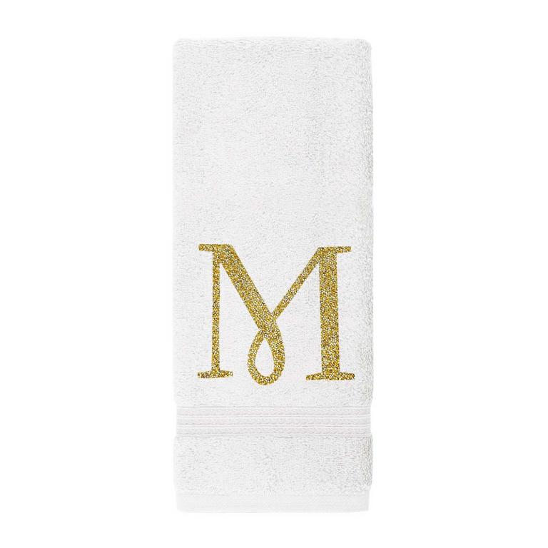 White plush cotton terry hand towel with a sparkling gold rhinestone monogram "M" and decorative horizontal stripes at the bottom.