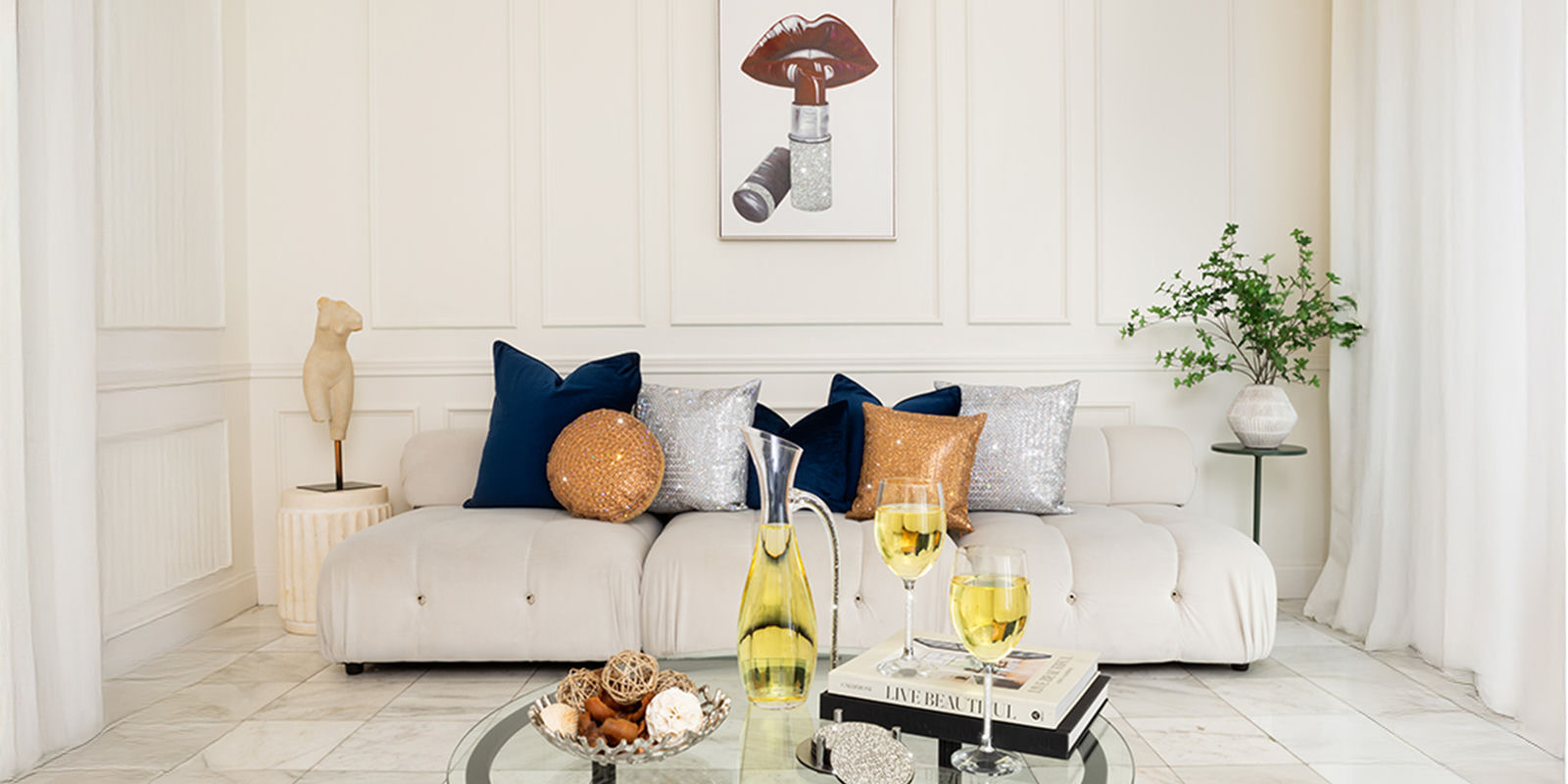 White&amp;&#x23;x20&#x3B;living&amp;&#x23;x20&#x3B;room&amp;&#x23;x20&#x3B;with&amp;&#x23;x20&#x3B;navy&amp;&#x23;x20&#x3B;and&amp;&#x23;x20&#x3B;metallic&amp;&#x23;x20&#x3B;accent&amp;&#x23;x20&#x3B;pillows&amp;&#x23;x20&#x3B;and&amp;&#x23;x20&#x3B;wine&amp;&#x23;x20&#x3B;on&amp;&#x23;x20&#x3B;a&amp;&#x23;x20&#x3B;glass&amp;&#x23;x20&#x3B;table