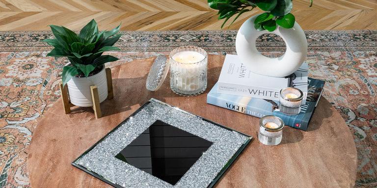 Styled round coffee table with candles, books, plants, and a mirrored tray