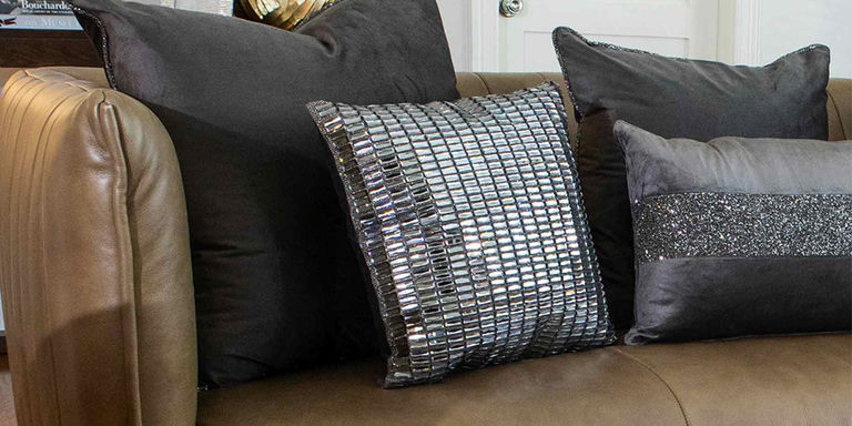 Silver mirrored and charcoal accent pillows on a brown leather sofa