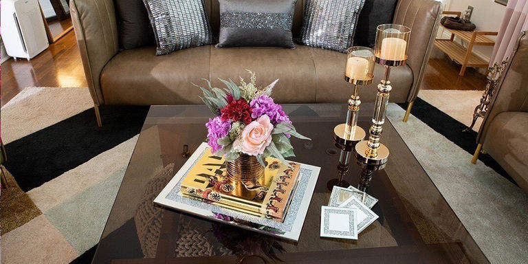 mesa de café con bandeja de espejo glamorosa, flores falsas, posavasos de pedrería y velas en una sala de estar de lujo