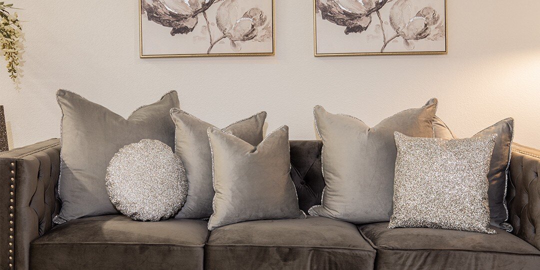 Gray&amp;&#x23;x20&#x3B;sectional&amp;&#x23;x20&#x3B;sofa&amp;&#x23;x20&#x3B;styled&amp;&#x23;x20&#x3B;with&amp;&#x23;x20&#x3B;multiple&amp;&#x23;x20&#x3B;throw&amp;&#x23;x20&#x3B;pillows&amp;&#x23;x20&#x3B;including&amp;&#x23;x20&#x3B;gray&amp;&#x23;x20&#x3B;velvet&amp;&#x23;x20&#x3B;pillows,&amp;&#x23;x20&#x3B;round&amp;&#x23;x20&#x3B;silver&amp;&#x23;x20&#x3B;sequined&amp;&#x23;x20&#x3B;pillow,&amp;&#x23;x20&#x3B;and&amp;&#x23;x20&#x3B;square&amp;&#x23;x20&#x3B;sparkly&amp;&#x23;x20&#x3B;silver&amp;&#x23;x20&#x3B;pillow,&amp;&#x23;x20&#x3B;with&amp;&#x23;x20&#x3B;two&amp;&#x23;x20&#x3B;framed&amp;&#x23;x20&#x3B;botanical&amp;&#x23;x20&#x3B;prints&amp;&#x23;x20&#x3B;hanging&amp;&#x23;x20&#x3B;above&amp;&#x23;x20&#x3B;and&amp;&#x23;x20&#x3B;greenery&amp;&#x23;x20&#x3B;accent&amp;&#x23;x20&#x3B;visible.