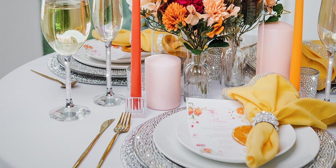 An&amp;&#x23;x20&#x3B;elegant&amp;&#x23;x20&#x3B;table&amp;&#x23;x20&#x3B;setting&amp;&#x23;x20&#x3B;featuring&amp;&#x23;x20&#x3B;warm&amp;&#x23;x20&#x3B;orange&amp;&#x23;x20&#x3B;and&amp;&#x23;x20&#x3B;yellow&amp;&#x23;x20&#x3B;tones.&amp;&#x23;x20&#x3B;The&amp;&#x23;x20&#x3B;place&amp;&#x23;x20&#x3B;setting&amp;&#x23;x20&#x3B;includes&amp;&#x23;x20&#x3B;white&amp;&#x23;x20&#x3B;plates&amp;&#x23;x20&#x3B;with&amp;&#x23;x20&#x3B;delicate&amp;&#x23;x20&#x3B;floral&amp;&#x23;x20&#x3B;patterns,&amp;&#x23;x20&#x3B;gold&amp;&#x23;x20&#x3B;flatware,&amp;&#x23;x20&#x3B;crystal&amp;&#x23;x20&#x3B;wine&amp;&#x23;x20&#x3B;glasses&amp;&#x23;x20&#x3B;filled&amp;&#x23;x20&#x3B;with&amp;&#x23;x20&#x3B;white&amp;&#x23;x20&#x3B;wine,&amp;&#x23;x20&#x3B;and&amp;&#x23;x20&#x3B;bright&amp;&#x23;x20&#x3B;yellow&amp;&#x23;x20&#x3B;cloth&amp;&#x23;x20&#x3B;napkins.&amp;&#x23;x20&#x3B;Orange&amp;&#x23;x20&#x3B;pillar&amp;&#x23;x20&#x3B;candles&amp;&#x23;x20&#x3B;in&amp;&#x23;x20&#x3B;glass&amp;&#x23;x20&#x3B;holders&amp;&#x23;x20&#x3B;and&amp;&#x23;x20&#x3B;a&amp;&#x23;x20&#x3B;centerpiece&amp;&#x23;x20&#x3B;of&amp;&#x23;x20&#x3B;orange&amp;&#x23;x20&#x3B;and&amp;&#x23;x20&#x3B;burgundy&amp;&#x23;x20&#x3B;flowers&amp;&#x23;x20&#x3B;in&amp;&#x23;x20&#x3B;clear&amp;&#x23;x20&#x3B;glass&amp;&#x23;x20&#x3B;vases&amp;&#x23;x20&#x3B;create&amp;&#x23;x20&#x3B;a&amp;&#x23;x20&#x3B;festive&amp;&#x23;x20&#x3B;fall&amp;&#x23;x20&#x3B;dining&amp;&#x23;x20&#x3B;atmosphere.&amp;&#x23;x20&#x3B;Sparkly&amp;&#x23;x20&#x3B;charger&amp;&#x23;x20&#x3B;plates&amp;&#x23;x20&#x3B;and&amp;&#x23;x20&#x3B;napkin&amp;&#x23;x20&#x3B;rings&amp;&#x23;x20&#x3B;add&amp;&#x23;x20&#x3B;glamorous&amp;&#x23;x20&#x3B;touches&amp;&#x23;x20&#x3B;to&amp;&#x23;x20&#x3B;the&amp;&#x23;x20&#x3B;seasonal&amp;&#x23;x20&#x3B;tablescape.