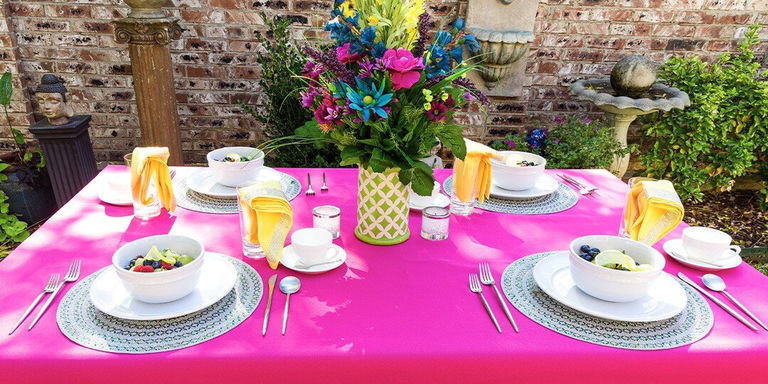 Outdoor dining setup featuring margarita glasses with blue rhinestone rims, turquoise beaded placemats, yellow napkins with sparkly napkin rings, and grilled corn on wooden slat table in natural lighting.