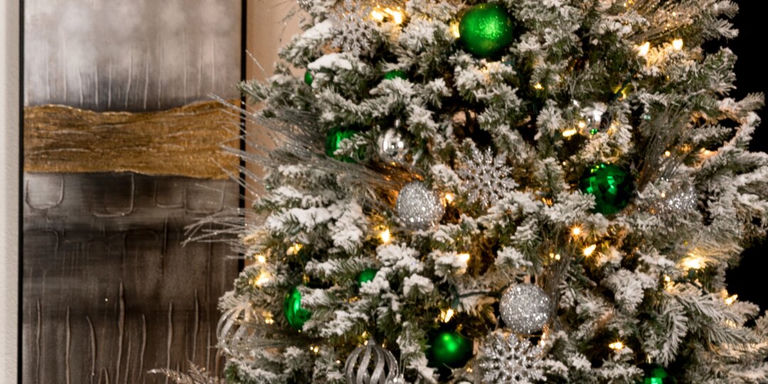 Flocked white Christmas tree adorned with emerald green glass ornaments, silver baubles, and glowing warm lights creating magical holiday ambiance