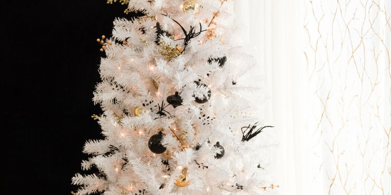 Elegant white flocked Christmas tree decorated with gold ornaments, pearl garlands, and warm twinkling lights against black backdrop