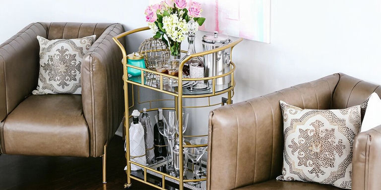 carrito de bar glamuroso con marco dorado, flores frescas y almohadas de strass en sillas de cuero