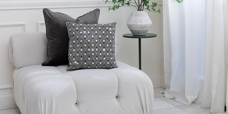 moderna silla blanca de acento con almohadas de terciopelo y rhinestones en un rincón de luz natural