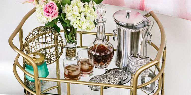 carrito de bar dorado estilizado con flores frescas, decantador de cristal, posavasos de strass y accesorios de cóctel