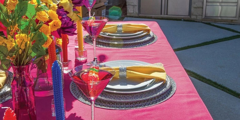 Outdoor glam dining table with pink velvet tablecloth, rhinestone chargers, and yellow napkins