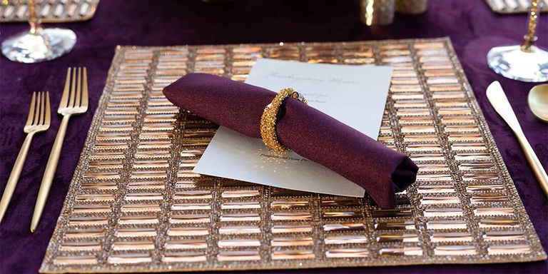 gold rhinestone placemat with purple napkin and gold napkin ring on rich table setting