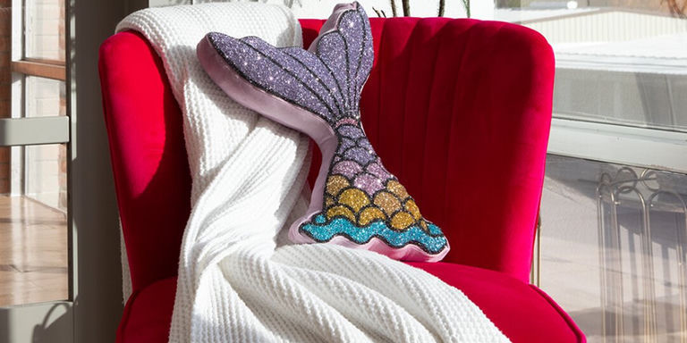 cojín de sirena rosa brillante con pedrería colocado en un sofá moderno neutral