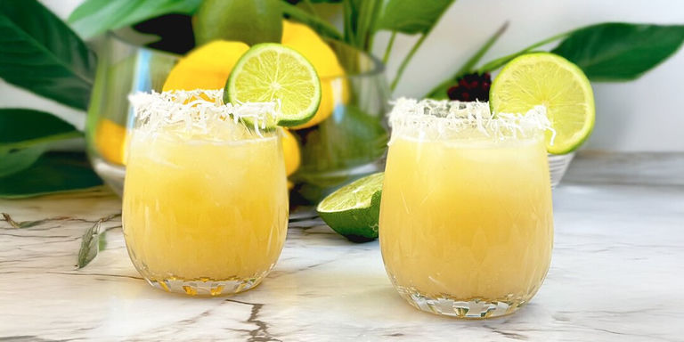 yellow coconut margaritas with shredded coconut rims and lime garnish on marble counter