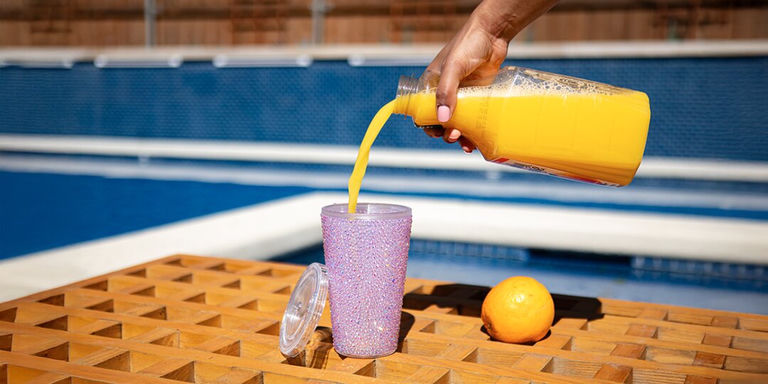 Pink rhinestone tumbler being filled with orange juice by swimming pool